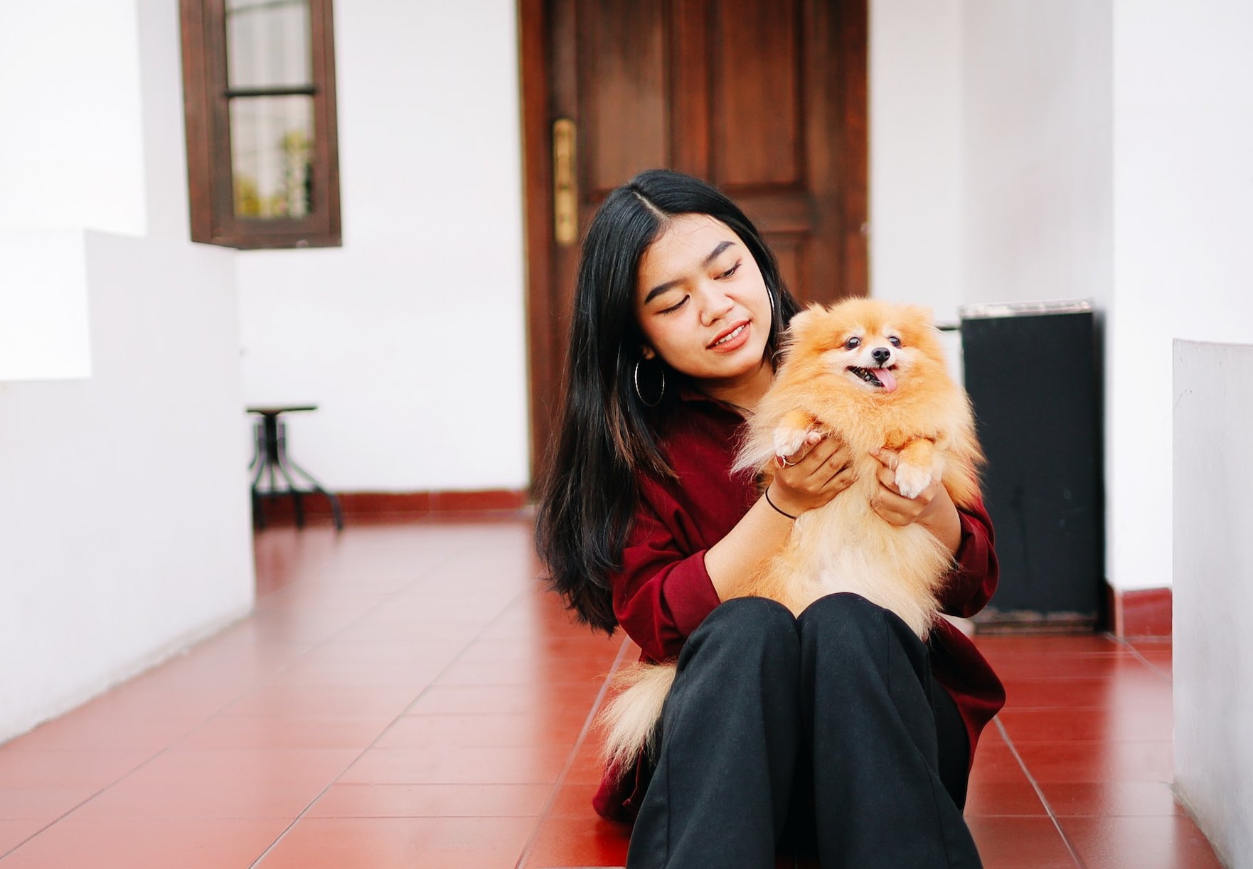 Girl and small dog sitting on red tile flooring